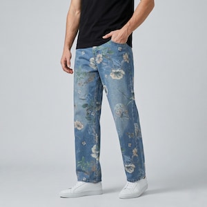 May include: Light blue denim jeans with a floral pattern in shades of white, beige, and green. The jeans have a straight leg cut and are worn with white sneakers. The model is wearing a black t-shirt.