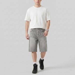 May include: A person wearing a white short-sleeve t-shirt, gray denim shorts, black high-top sneakers, and a silver watch. The shorts have a distressed look with a raw hem and white paint splatters.