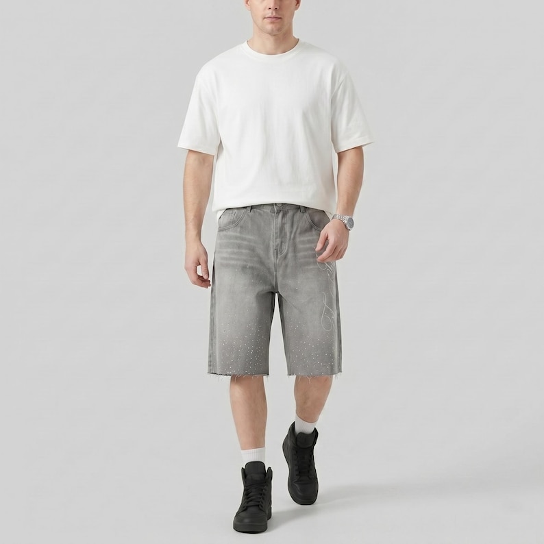 May include: A person wearing a white short-sleeve t-shirt, gray denim shorts, black high-top sneakers, and a silver watch. The shorts have a distressed look with a raw hem and white paint splatters.