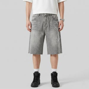 May include: Gray denim shorts with a raw hem and white splatter paint effect. The shorts feature a white decorative design on the right leg. The model is wearing black high-top sneakers and a white t-shirt.