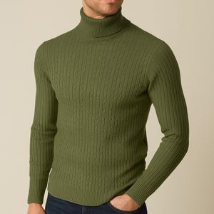 May include: Olive green turtleneck sweater with a cable knit design. The long-sleeved sweater has a ribbed collar and cuffs. The model is wearing dark blue jeans. The sweater is made of a soft, comfortable material.