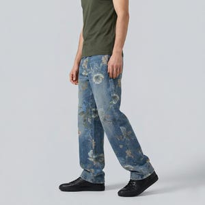 May include: Light blue denim jeans with a floral pattern in shades of white, green, and blue. The jeans have a straight leg cut. The person in the image is wearing a green t-shirt and black sneakers.