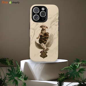 Puede incluir: Funda de teléfono con un diseño que presenta un personaje parecido a Dobby, un búho y libros. La funda tiene un fondo crema con aspecto de mármol. El búho está posado debajo del personaje, con el escudo de Hogwarts en la parte inferior.