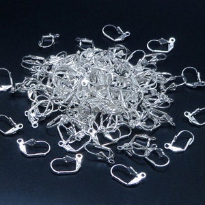 May include: A large pile of silver earring hooks. The hooks are made of metal and have a simple design.