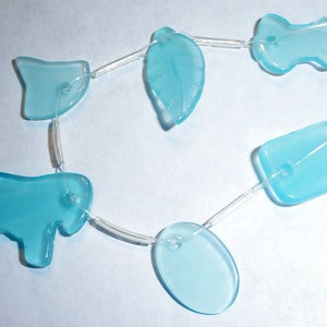 May include: A string of light blue glass beads in various shapes, including a leaf, a rectangle, an oval, a horse, and a bone. The beads are strung on a clear string.
