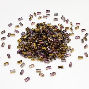 May include: A large pile of iridescent gold and purple glass beads in a rectangular shape. The beads are scattered around the pile.