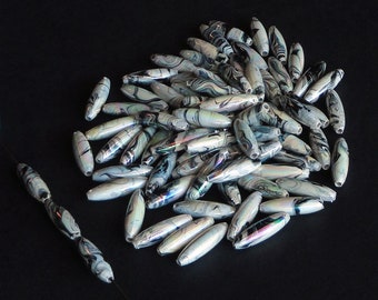 May include: A large pile of white and black marbled oval beads. The beads have a iridescent sheen and are approximately 1 inch long.