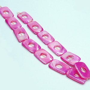 May include: A strand of pink shell beads with square shapes and a hole in the center of each bead.
