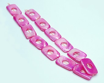 May include: A strand of pink shell beads with square shapes and a hole in the center of each bead.