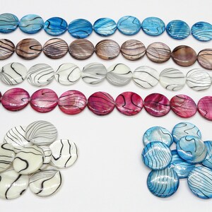 May include: A collection of round, flat, decorative beads with various patterns. The beads are made of mother of pearl and have a white, blue, pink, and brown color scheme. The beads are arranged in a line and in a pile.