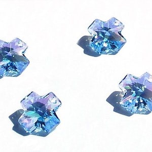 Puede incluir: Cuatro abalorios de cruz de cristal azul claro con un diseño facetado.