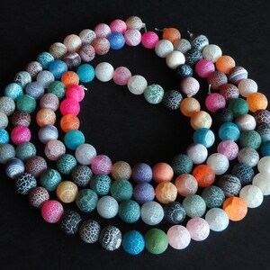 May include: A strand of colorful agate beads with a white, translucent, and crackled finish. The beads are round and have a variety of colors, including pink, blue, green, orange, and purple.