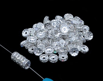 May include: A large pile of silver-toned round beads with clear rhinestones. The beads have a hole in the center and are designed for jewelry making.