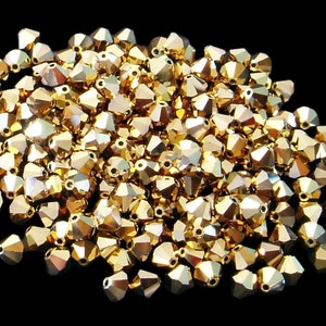 May include: A large pile of gold-colored glass beads. The beads are faceted and have a shiny finish.