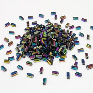 May include: A large pile of iridescent, rectangular glass beads in shades of blue, green, and purple. The beads are scattered on a white surface.