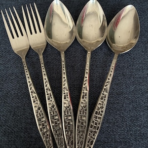 May include: A set of two silver-toned metal forks and three silver-toned metal spoons. Each piece of cutlery features a textured, mosaic-like pattern of raised geometric shapes along the handle, contrasting with the smooth, polished finish of the bowls and tines.