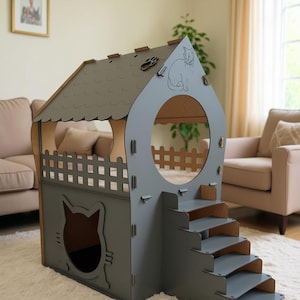 May include: A gray wooden cat house with a house-shaped design. Features include a cat-shaped doorway, a round window, and a small staircase. The roof has a paw print and a cat silhouette. The house sits on a white rug.