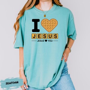 A woman wearing a turquoise t-shirt with a graphic design that says "I ♥ JESUS JESUS YOU" and features a heart-shaped waffle.