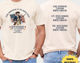 May include: Ivory-colored t-shirt featuring a patriotic design commemorating the 250th anniversary of the United States. The front displays a soldier with a flag and text "Descendant of a Patriot." The back lists names and dates.