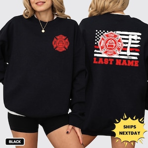 May include: A black crewneck sweatshirt featuring a red fire department emblem on the left chest. The back displays a large graphic of a stylized American flag with a red line, a fire department emblem, an axe, and the text LAST NAME.