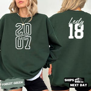 May include: Forest green sweatshirt with white text reading "20 Limited Edition 07" on the front. The back of the sweatshirt has the name "Lesly" and the number "18" in white. The sweatshirt is a casual style.