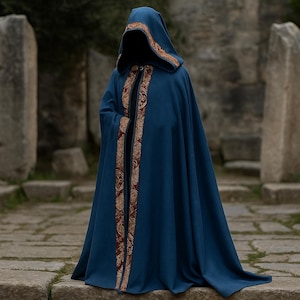 May include: A hooded, dark blue cloak with ornate gold trim. The cloak features a long, flowing design and is worn in an outdoor setting. The trim is detailed with a repeating pattern. The cloak is a medieval or fantasy-themed garment.