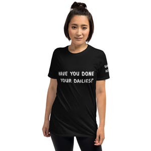 May include: A black t-shirt with the text "HAVE YOU DONE YOUR DAILIES?" in white. The shirt is worn by a person with dark hair. The letters "GA AD" are printed on the right sleeve.