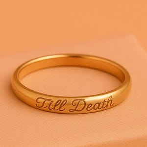 May include: A gold-colored ring with the inscription "Till Death" is displayed on a peach-colored box. The ring is circular and has a smooth surface. The box has the word "RIOLUXEUS" printed on it.