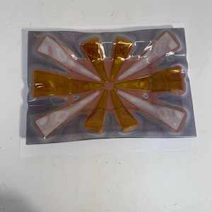 May include: Rectangular glass dish with a sunburst design. The dish features a gray background with a central sunburst pattern in gold and white. The sunburst design radiates from the center, creating a striking visual effect. The dish is likely used for decorative purposes.