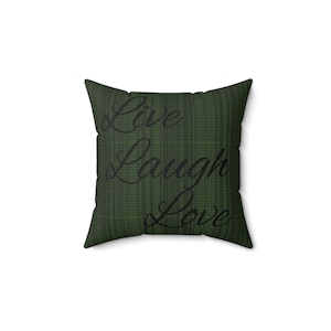 Może przedstawiać: Kwadratowa poduszka dekoracyjna z ciemnozielonym, teksturowanym tłem. Słowa "Live Laugh Love" są wydrukowane czarną czcionką na przodzie. Poduszka jest kwadratowa i wydaje się być wykonana z miękkiej tkaniny.