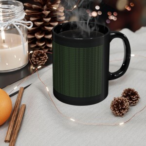 May include: A black ceramic coffee mug with a green binary code design. The mug is filled with a dark liquid, and steam rises from the top. The mug sits on a light gray surface with decorative elements.
