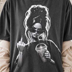 Może przedstawiać: Ciemnoszary t-shirt z czarno-białą grafiką przedstawiającą osobę z wysokim kokiem, w okularach przeciwsłonecznych, trzymającą plastikowy kubek z mrożoną kawą i słomką oraz wykonującą gest środkowego palca.