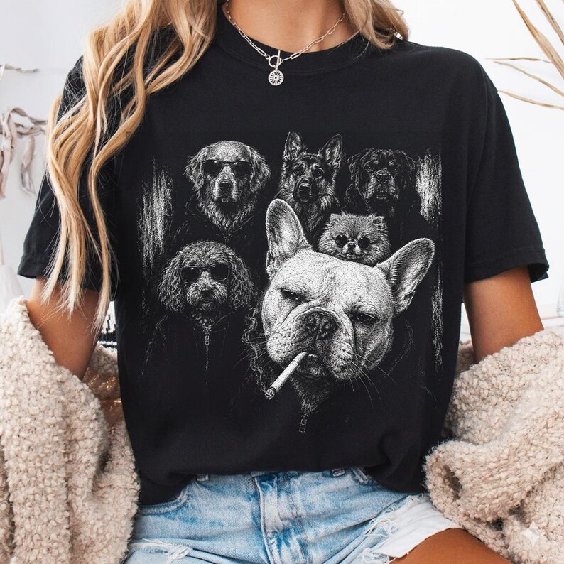 May include: A black short-sleeved t-shirt featuring a white graphic print of several dog breeds, including a French Bulldog with a cigarette in its mouth, a Golden Retriever, a German Shepherd, a Rottweiler, a Poodle, and a small Pomeranian.