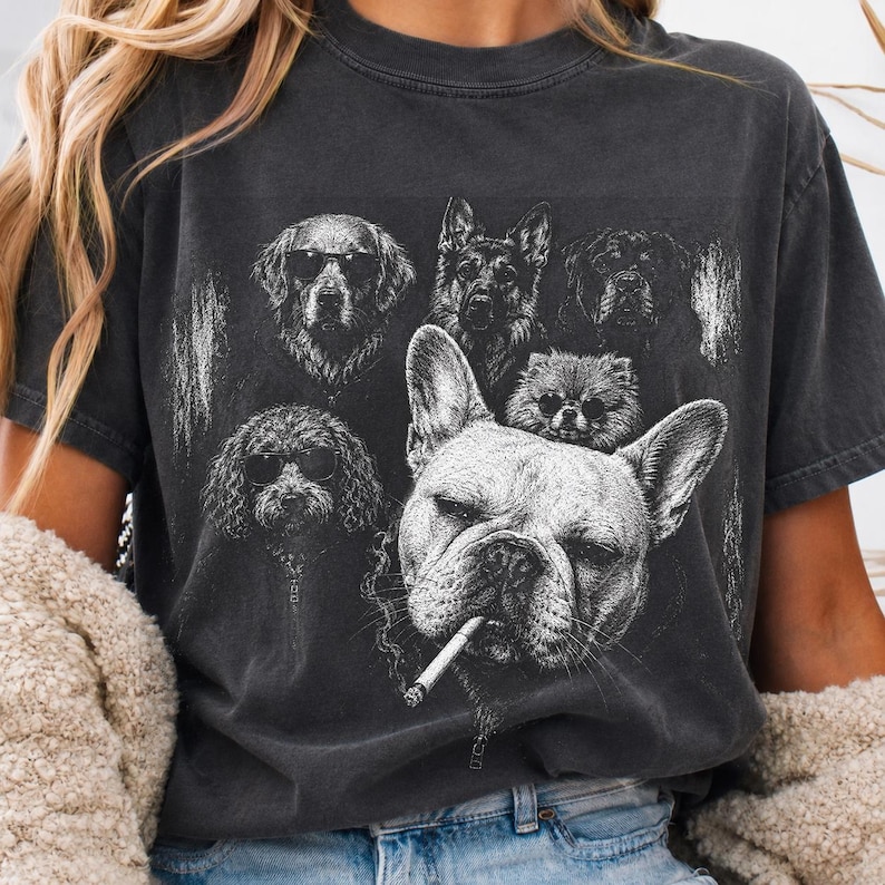May include: A charcoal gray crew neck t-shirt featuring a white graphic print of several dog breeds. The central image is a French Bulldog with a cigarette in its mouth, surrounded by other dogs including a Golden Retriever and a German Shepherd.