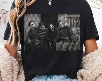 May include: A black short-sleeved t-shirt featuring a monochromatic graphic print of five iconic horror movie characters sitting together. The design depicts Michael Myers, Freddy Krueger, Ghostface, Jason Voorhees, and Chucky in a detailed illustration.