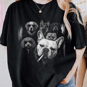 May include: A black short-sleeve t-shirt featuring a white graphic print of five dogs. The design includes a large French Bulldog in the foreground with a cigarette in its mouth, surrounded by four other dogs wearing hoodies and sunglasses.