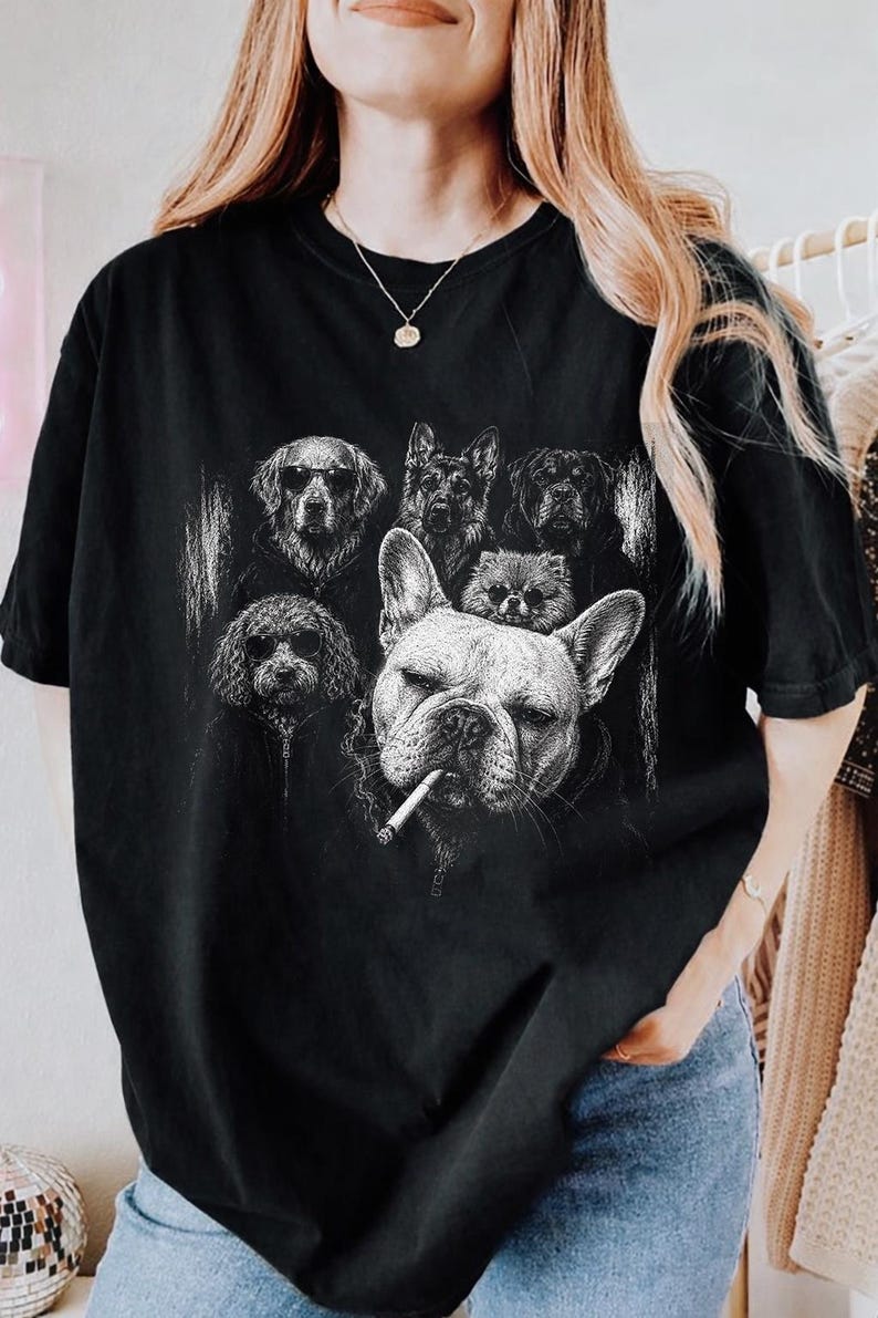 May include: A black short-sleeve t-shirt featuring a white graphic print of five dogs. The design includes a large French Bulldog in the foreground with a cigarette in its mouth, surrounded by four other dogs wearing hoodies and sunglasses.