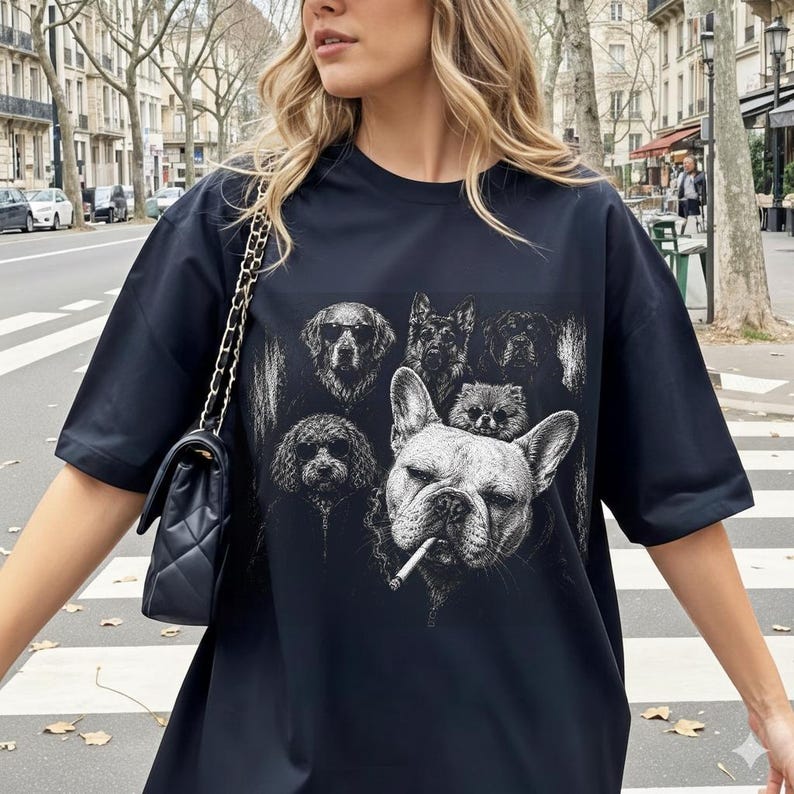 May include: A black short-sleeved t-shirt featuring a graphic print of several dog breeds, including a prominent French Bulldog with a cigarette in its mouth. The shirt is paired with a black quilted shoulder bag with a gold chain strap.