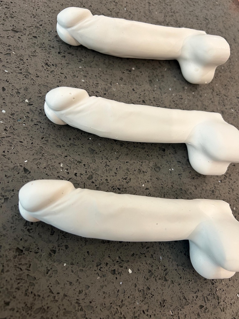 May include: Three white, phallic-shaped objects made of a smooth, matte material. Each piece features a rounded head, a cylindrical shaft, and a base with two rounded protrusions. The items are arranged in a parallel formation, showing a uniform design.