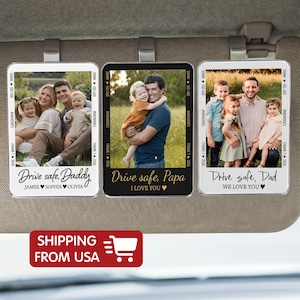 May include: Three car visor clips with family photos. Each clip has a different photo and message: "Drive safe, Daddy," "Drive safe, Papa," and "Drive safe, Dad." The clips have a black and white border with the text "#MEMORIES" and "FRAME 1 2026."