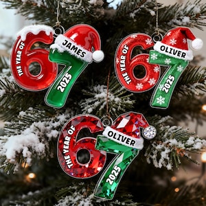 May include: Christmas tree ornaments shaped like the number 67, with a Santa hat on top. The ornaments are red and green, with the text "THE YEAR OF" and "2025". Some ornaments have names like "JAMES" and "OLIVER".