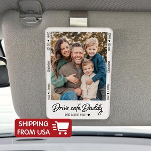 May include: A rectangular car visor photo holder with a family portrait. The photo holder has the text "Drive safe, Daddy, We love you" and "#MEMORIES". The visor clip is silver.