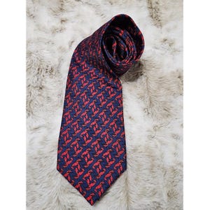 May include: A navy blue tie with a repeating red lobster pattern. The tie is made of a smooth fabric and is displayed on a textured, light-colored surface. The lobster design is evenly spaced across the tie.