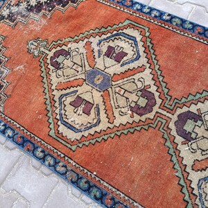 May include: An orange and blue vintage rug with a central geometric design. The rug features a detailed pattern with cream, purple, and green accents. The border is a dark blue with a repeating pattern. The rug is rectangular.
