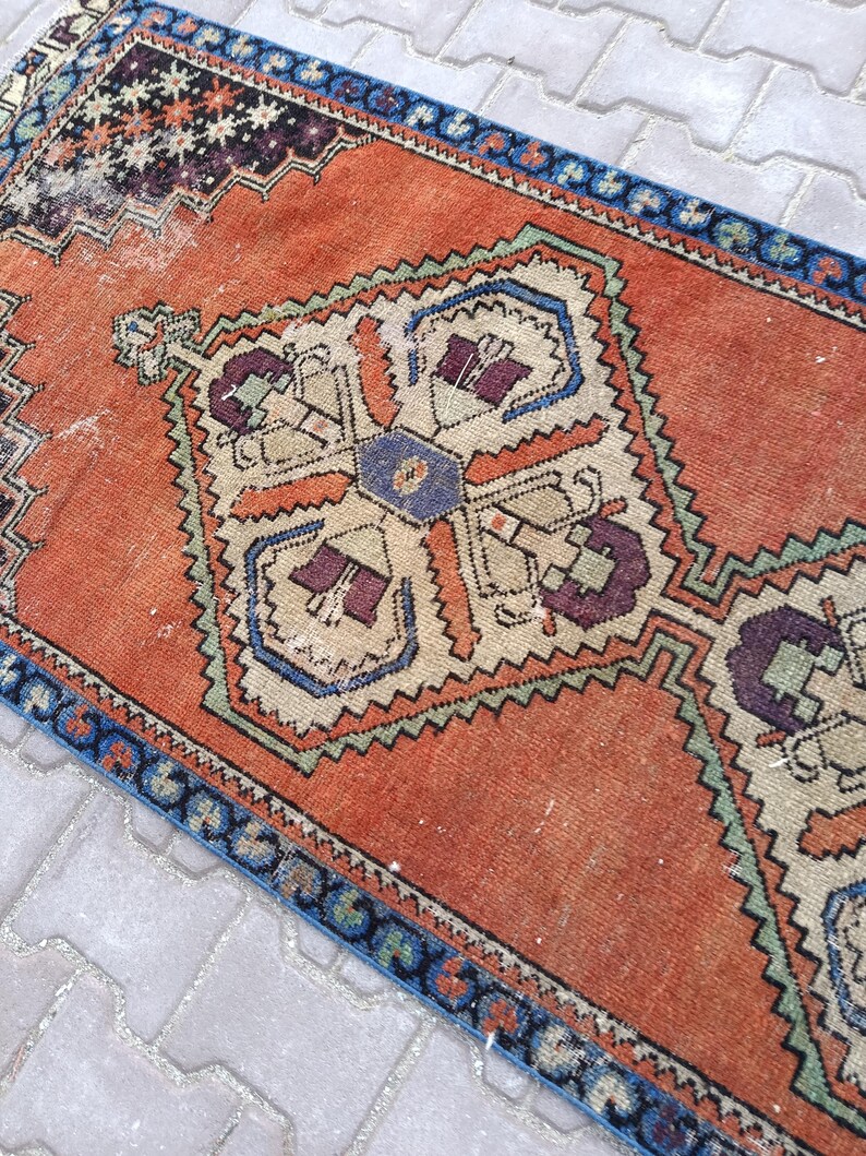 May include: An orange and blue vintage rug with a central geometric design. The rug features a detailed pattern with cream, purple, and green accents. The border is a dark blue with a repeating pattern. The rug is rectangular.