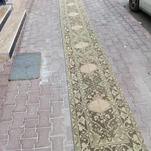 Peut inclure: Un long tapis rectangulaire avec un motif détaillé de motifs floraux et géométriques beiges et bruns. Le tapis est posé sur une surface en briques et semble être à l'extérieur. Le tapis a une bordure avec un motif répétitif.