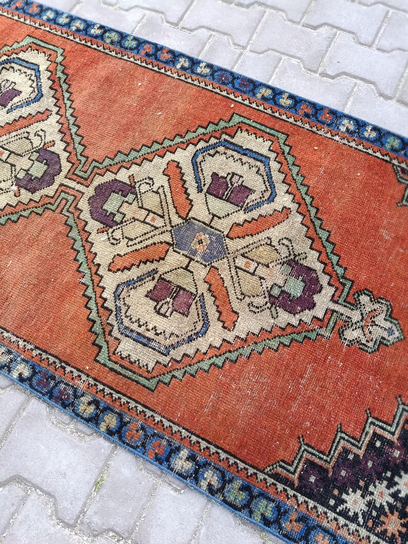 May include: An orange and blue vintage runner rug with geometric patterns. The rug features a central design with cream, purple, and orange details, framed by a blue border. The rug's design is symmetrical and detailed.