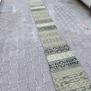 Könnte beinhalten: Ein langer, schmaler Teppich mit geometrischem Muster in Grau-, Schwarz- und Beigetönen. Der rechteckige Teppich hat ein gewebtes Design mit sich wiederholenden Mustern und Streifen. Ideal für einen Flur oder Eingangsbereich, das Design ist traditionell.
