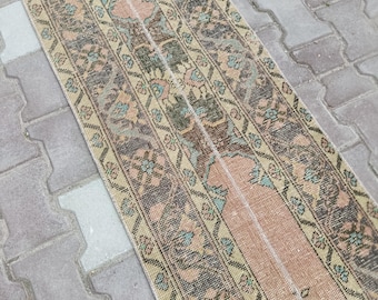 May include: A rectangular, vintage-style rug with a central peach-colored stripe flanked by patterned borders. The borders feature floral and geometric designs in shades of brown, green, and beige. The rug is likely made of woven material.