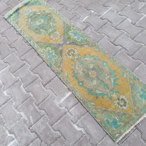 Könnte beinhalten: Ein rechteckiger Vintage-Teppich mit einem zentralen Medaillon-Design. Der Teppich hat einen warmgelben Hintergrund mit türkisen, grünen und violetten Akzenten. Die Ränder des Teppichs sind leicht ausgefranst.